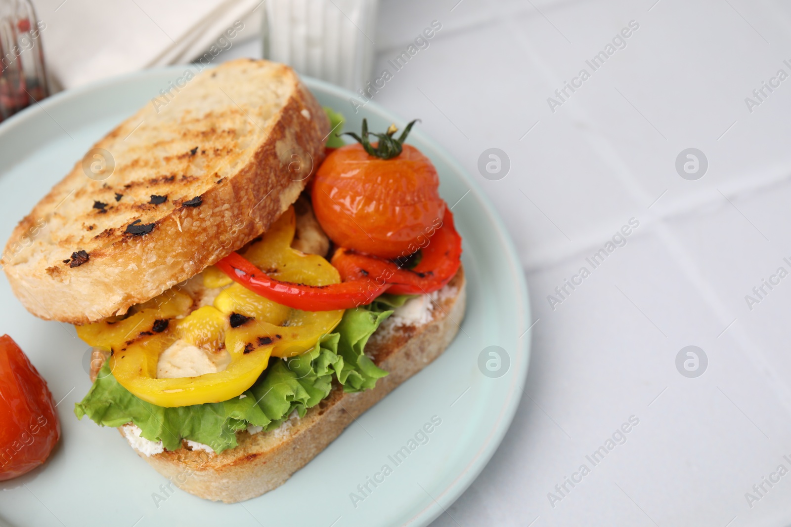 Photo of Tasty sandwich with grilled vegetables and cream cheese on white tiled table, closeup. Space for text