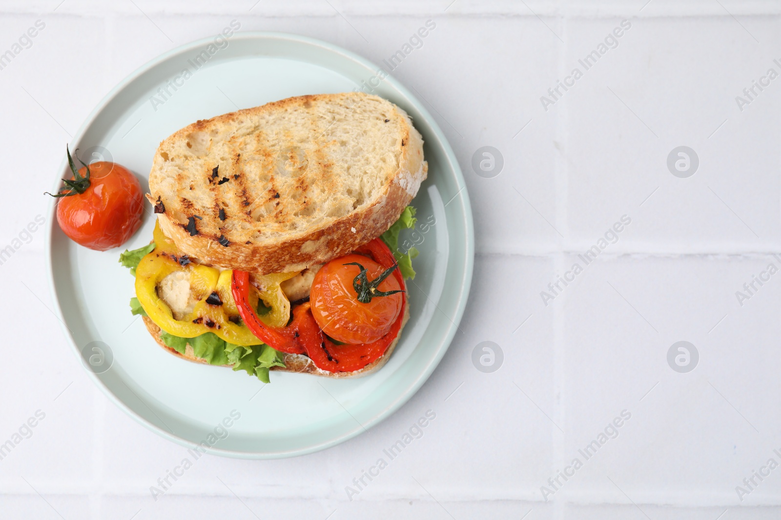 Photo of Tasty sandwich with grilled vegetables on white tiled table, top view. Space for text