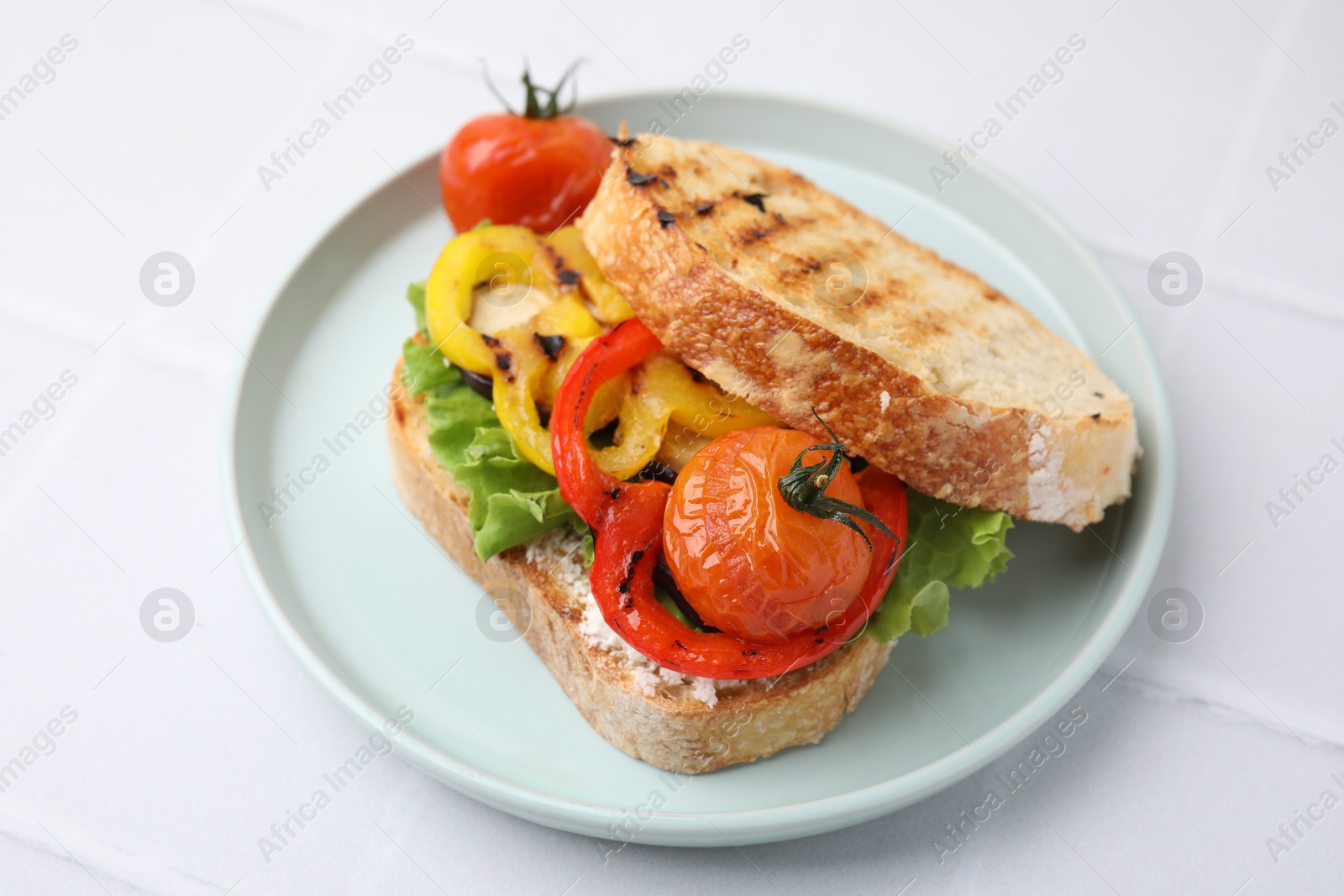 Photo of Tasty sandwich with grilled vegetables and cream cheese on white tiled table, closeup