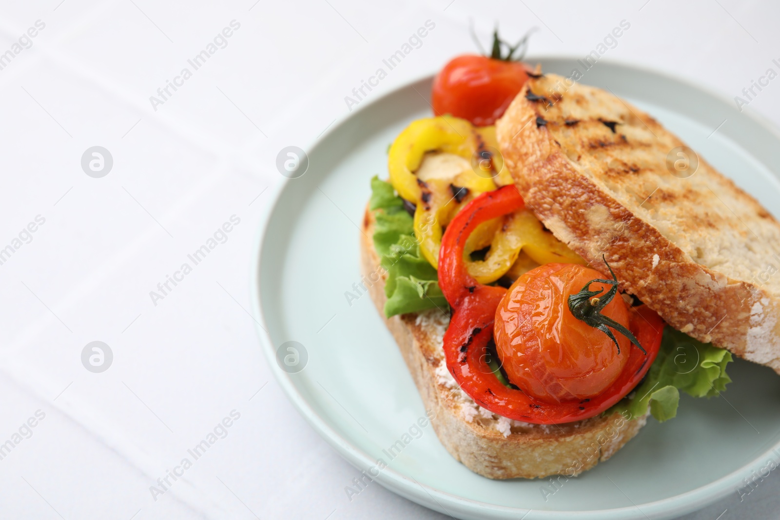 Photo of Tasty sandwich with grilled vegetables and cream cheese on white tiled table, closeup. Space for text