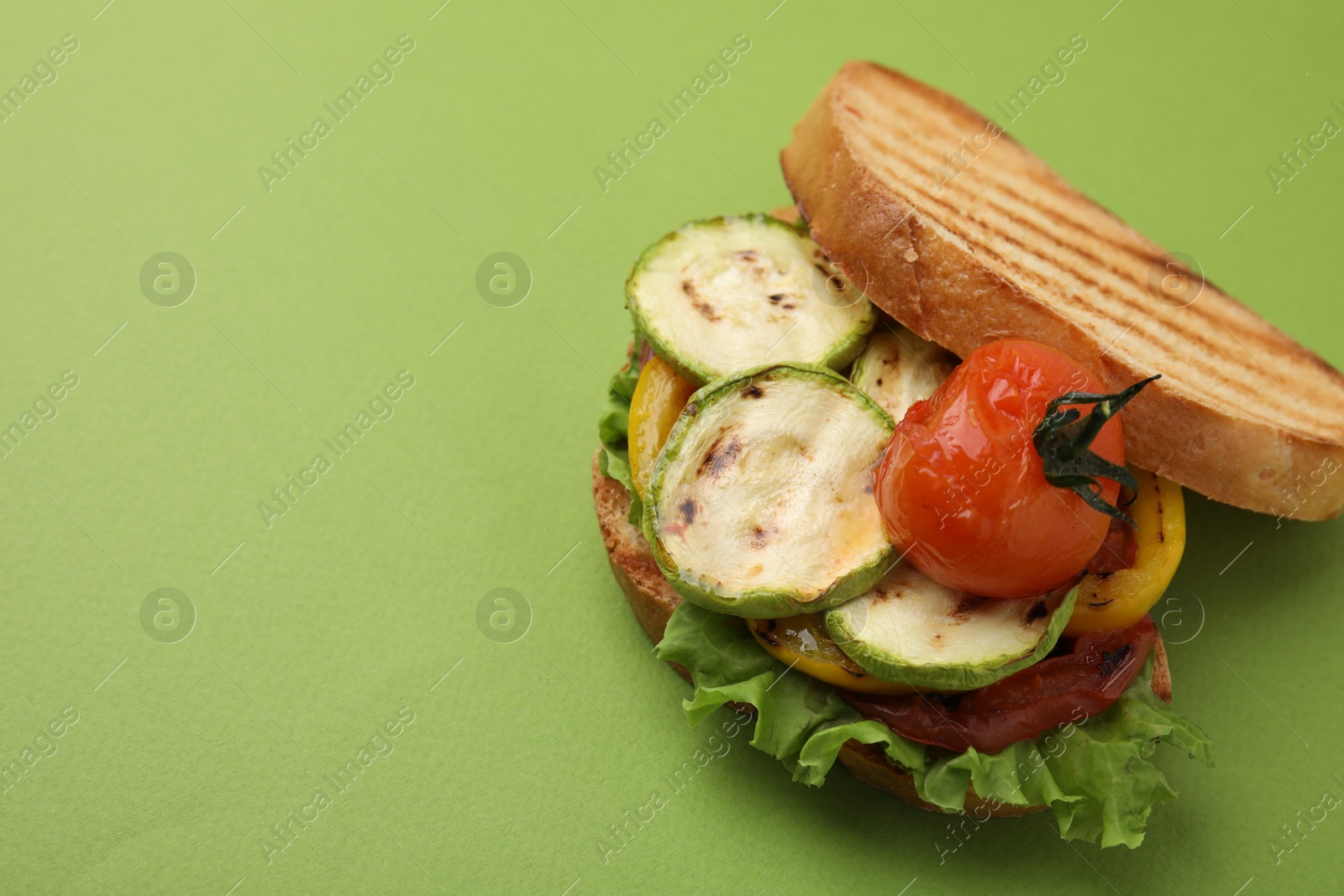 Photo of Tasty sandwich with grilled vegetables on green background, closeup. Space for text