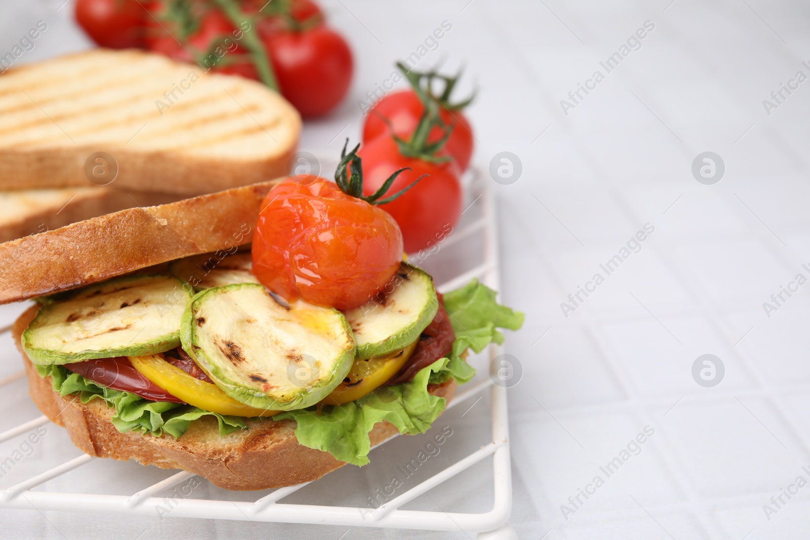 Photo of Tasty sandwich with grilled vegetables on white tiled table, closeup. Space for text