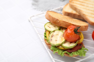 Photo of Tasty sandwich with grilled vegetables on white tiled table, closeup. Space for text