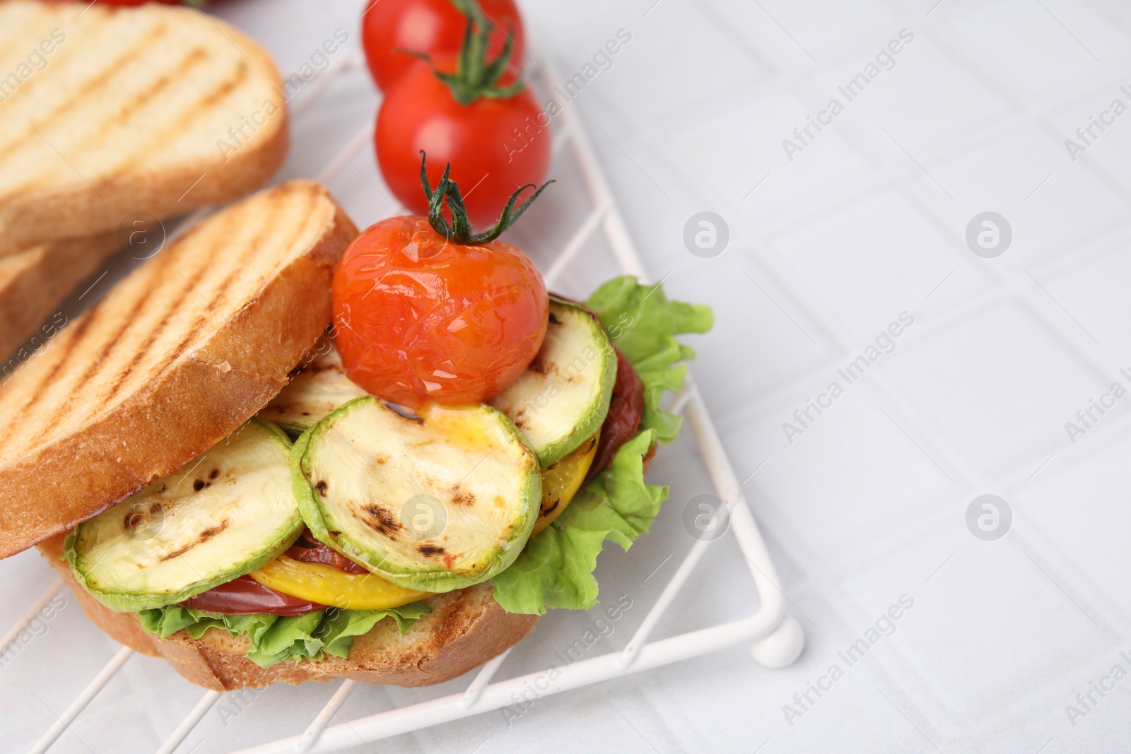 Photo of Tasty sandwich with grilled vegetables on white tiled table, closeup. Space for text