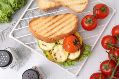 Photo of Tasty sandwich with grilled vegetables, fresh ones and spices on white tiled table, flat lay