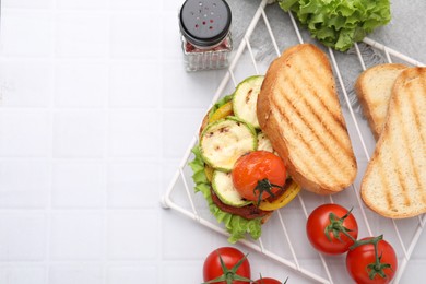 Photo of Tasty sandwich with grilled vegetables and fresh ones on white tiled table, flat lay. Space for text