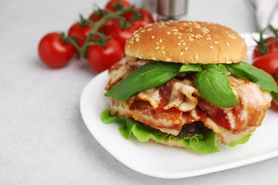 Photo of Delicious burger with bacon, greens and tomatoes on light table, closeup