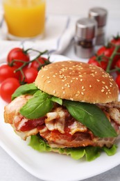 Delicious burger with bacon, greens and tomatoes on light table, closeup