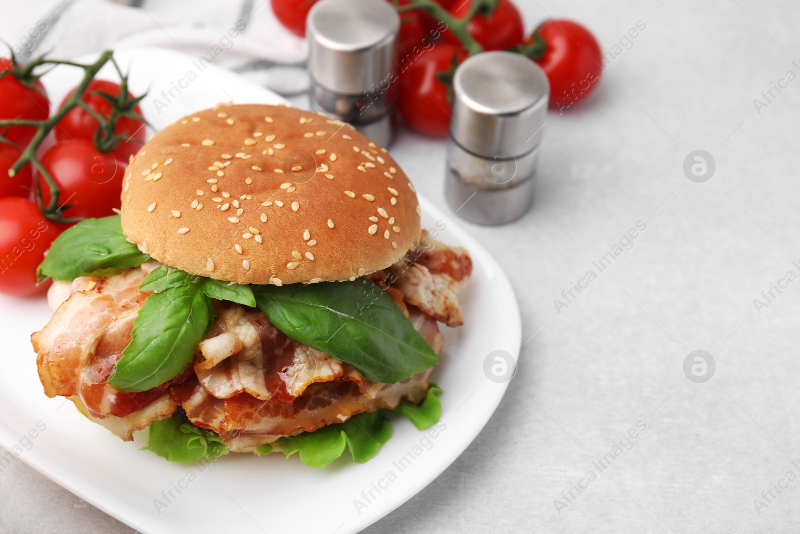 Photo of Delicious burger with bacon, greens and tomatoes on light table. Space for text