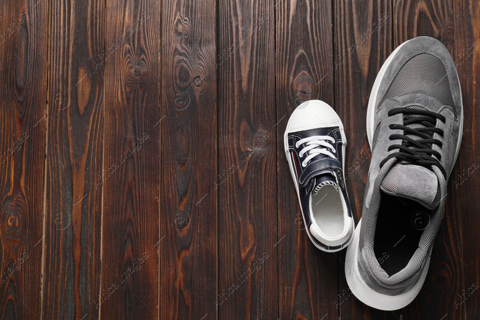 Photo of Big and small shoes on wooden table, top view. Space for text