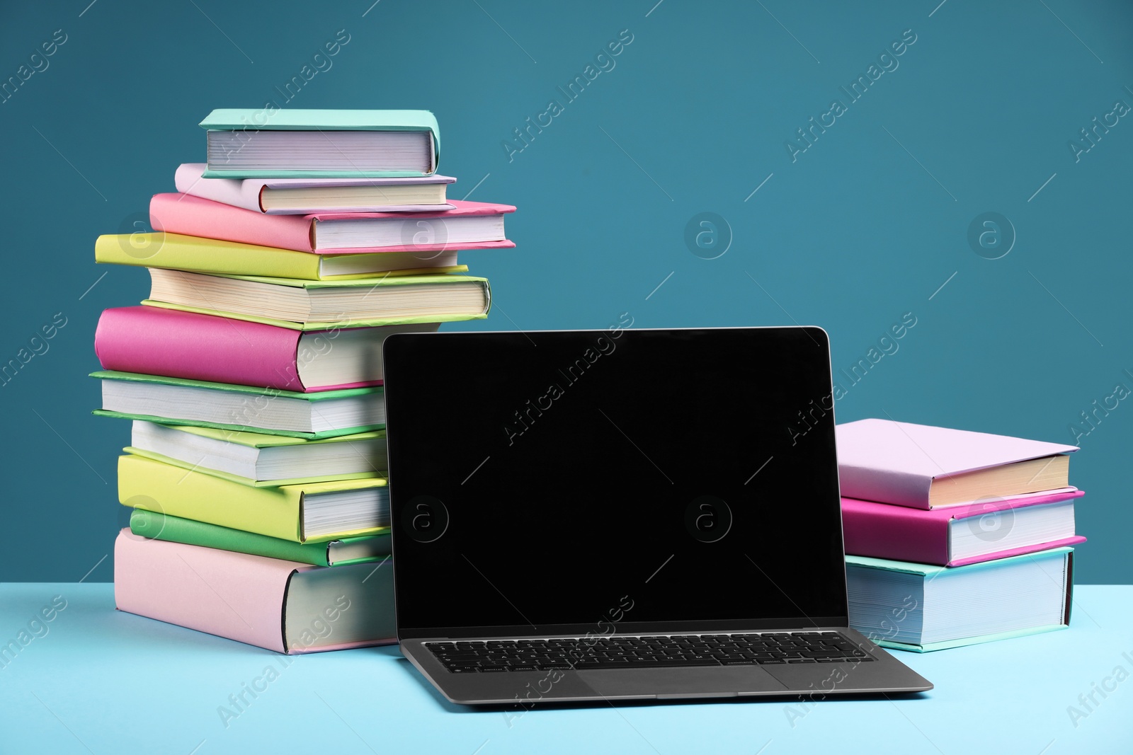 Photo of Stacks of colorful books and laptop on light blue background