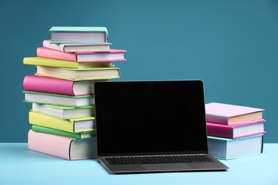 Stacks of colorful books and laptop on light blue background