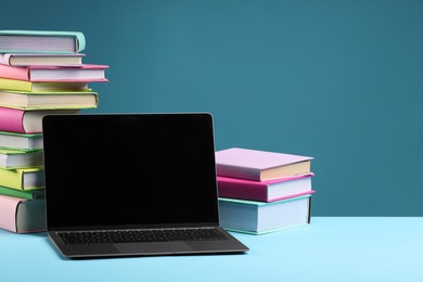 Photo of Stack of colorful books and laptop on light blue background, space for text