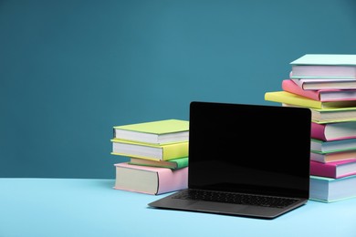 Photo of Stack of colorful books and laptop on light blue background, space for text