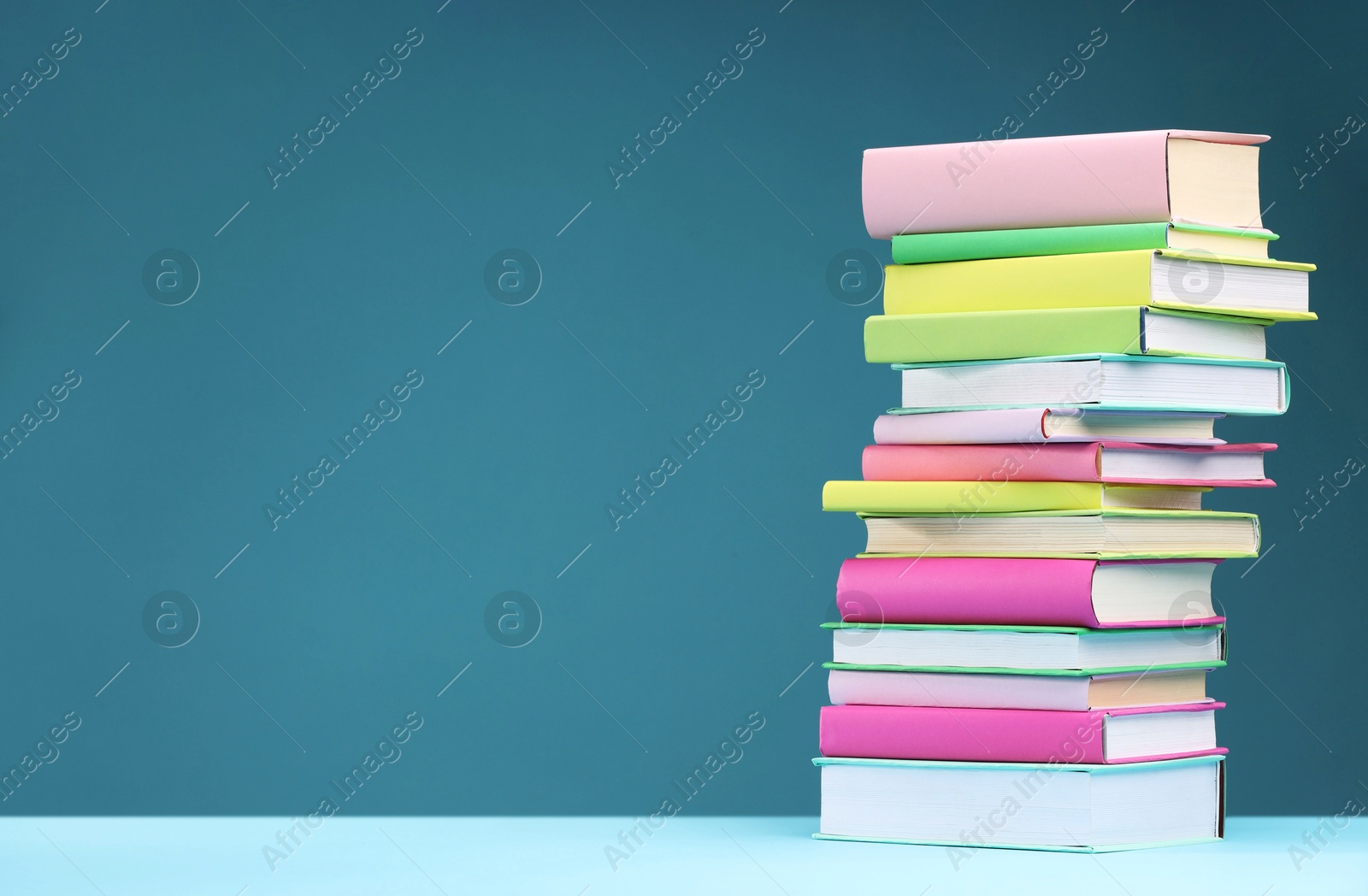 Photo of Stack of colorful books on light blue background, space for text