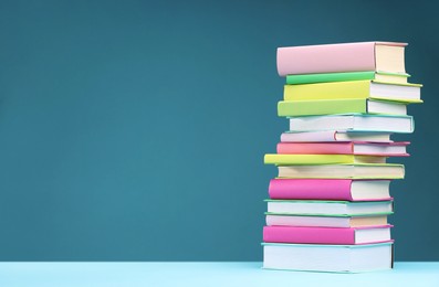 Stack of colorful books on light blue background, space for text