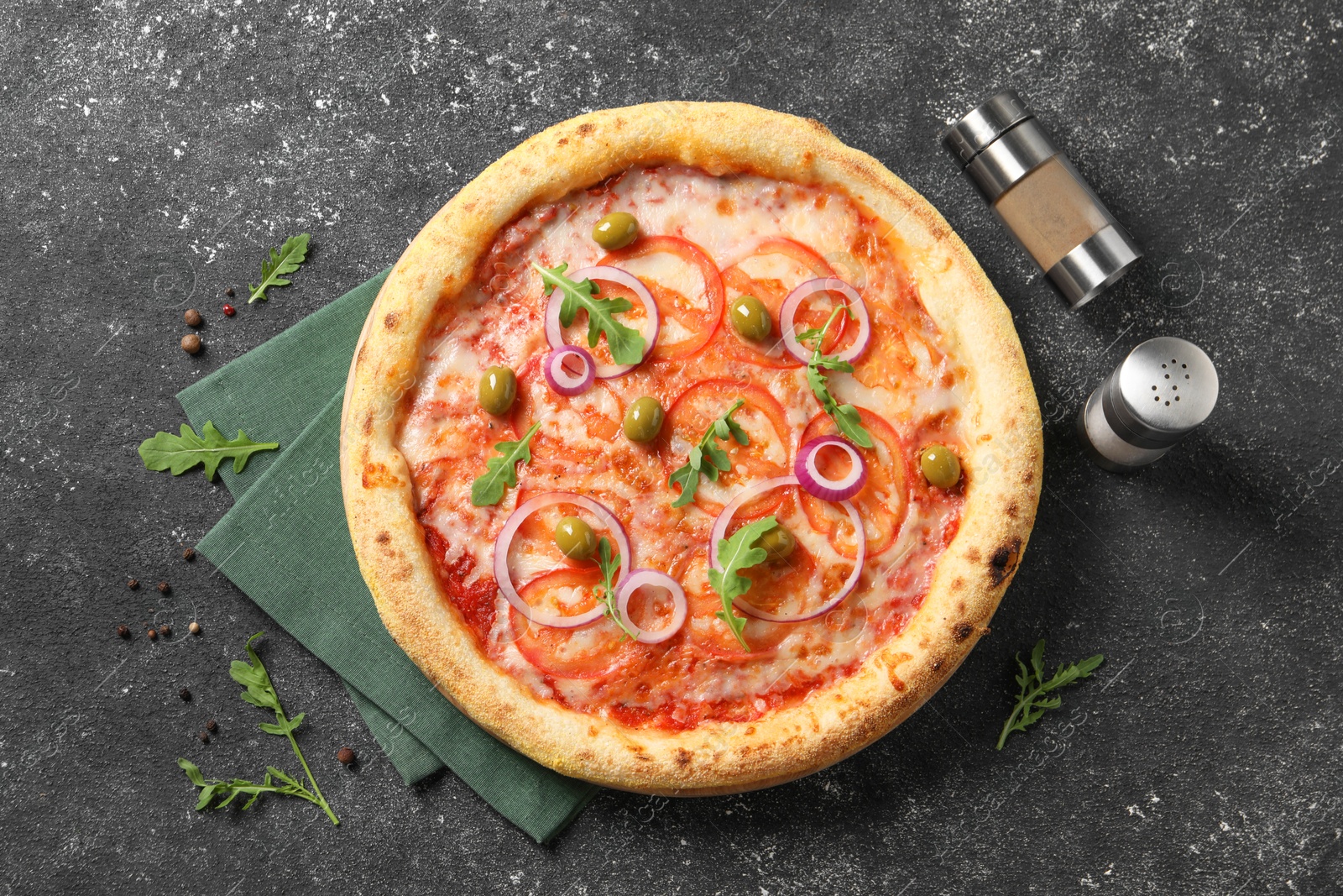 Photo of Delicious vegetarian pizza with arugula, salt and pepper on black table, top view