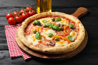 Photo of Delicious vegetarian pizza, oil and tomatoes on black wooden table