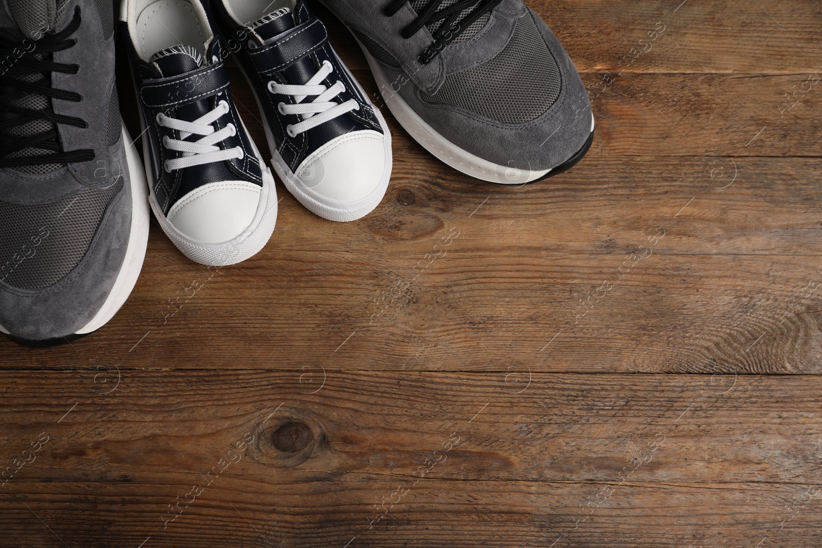 Photo of Big and small sneakers on wooden surface, flat lay. Space for text