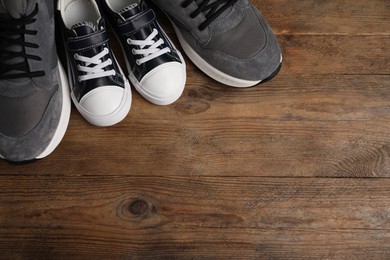 Photo of Big and small sneakers on wooden surface, flat lay. Space for text