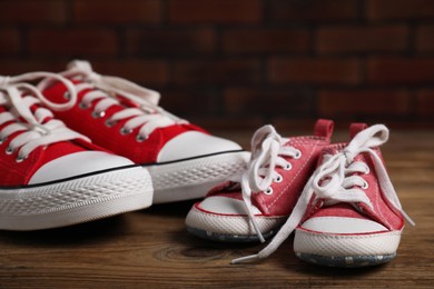 Photo of Big and small sneakers on wooden surface, closeup