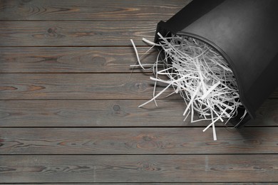 Photo of Shredded paper strips in bin on wooden table, space for text