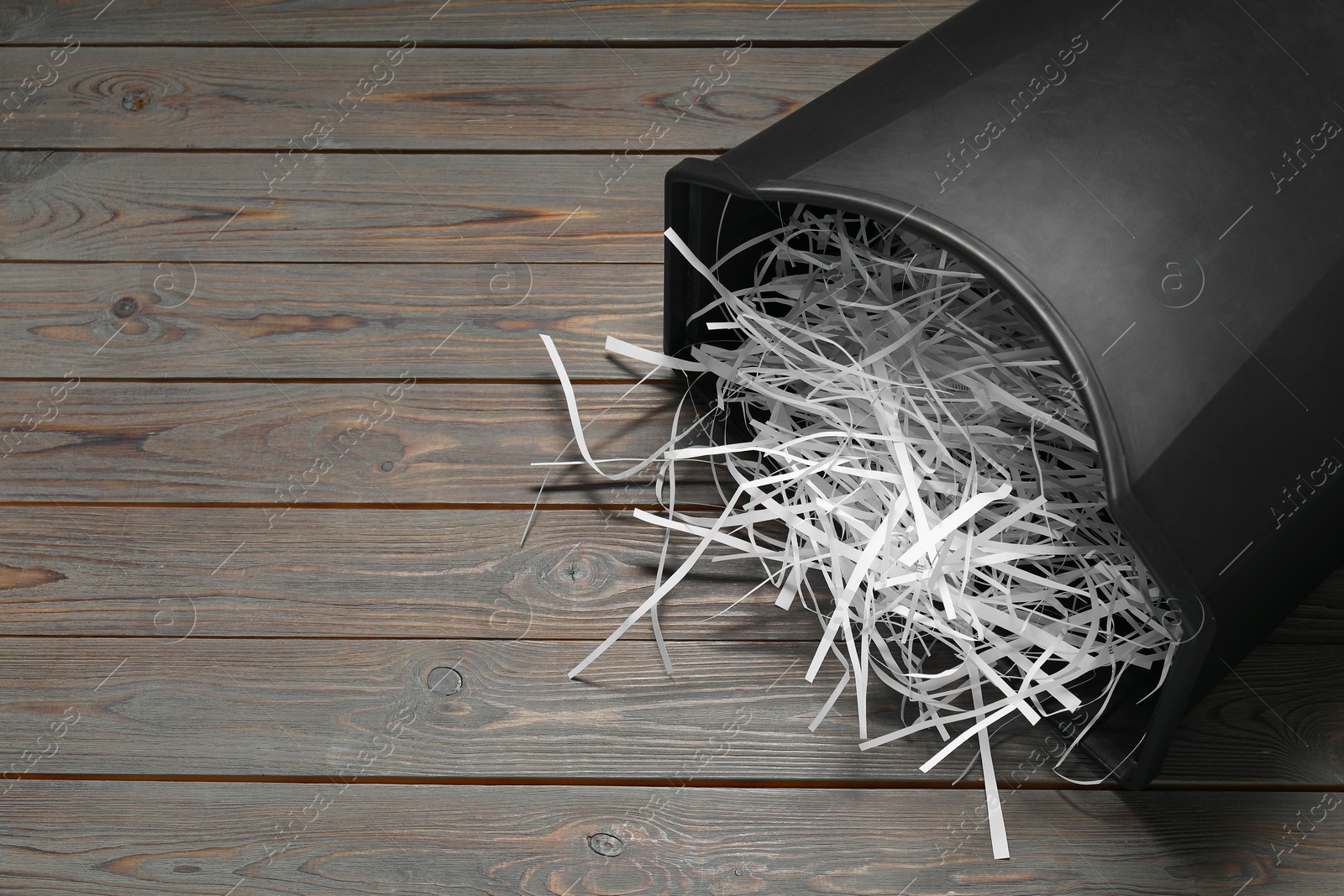 Photo of Shredded paper strips in bin on wooden table, space for text