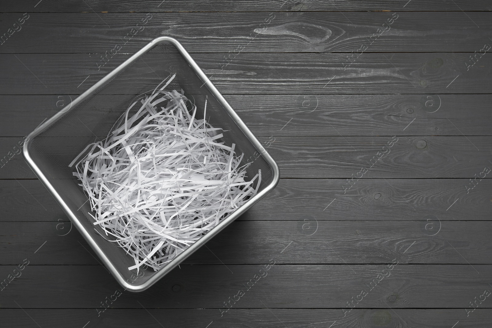 Photo of Shredded paper strips in trash bin on grey wooden table, top view. Space for text