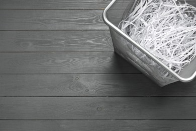 Photo of Shredded paper strips in trash bin on grey wooden table, top view. Space for text