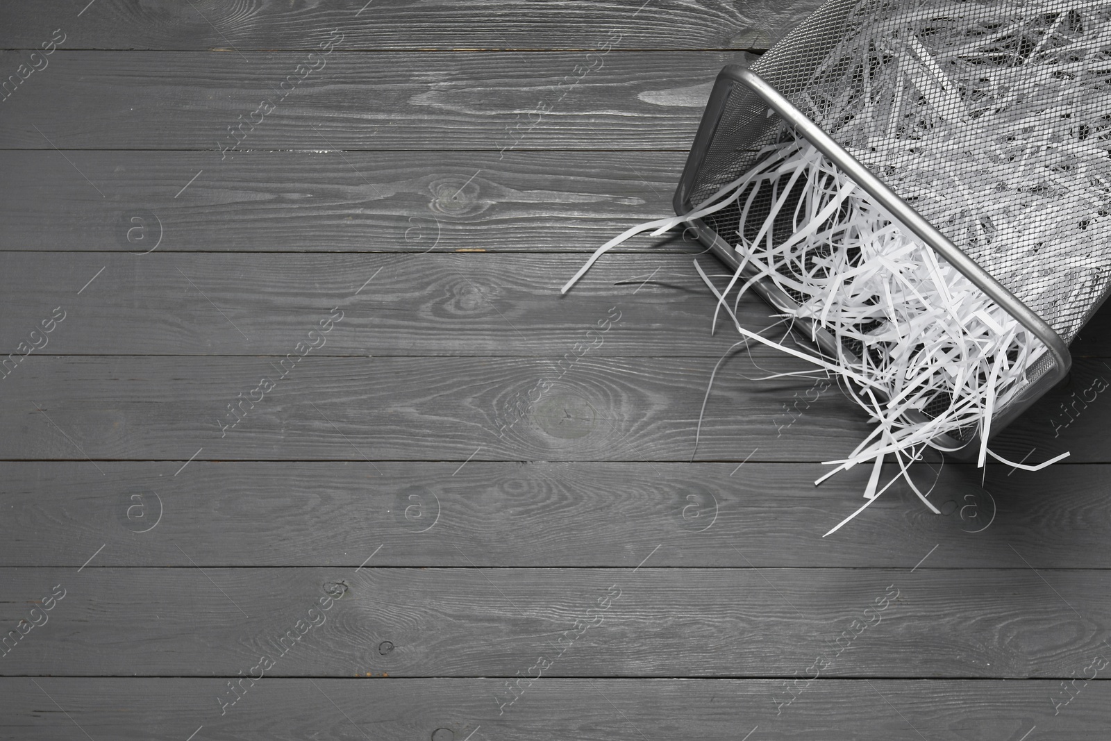 Photo of Shredded paper strips in trash bin on grey wooden table, top view. Space for text