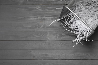 Photo of Shredded paper strips in trash bin on grey wooden table, top view. Space for text