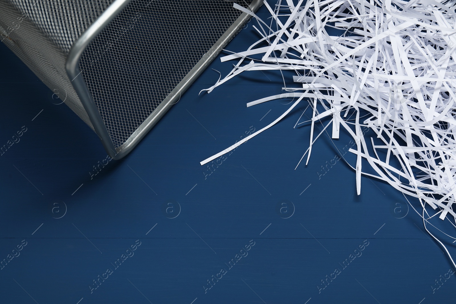 Photo of Shredded paper strips and trash bin on blue wooden table. Space for text