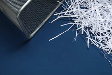 Shredded paper strips and trash bin on blue wooden table. Space for text