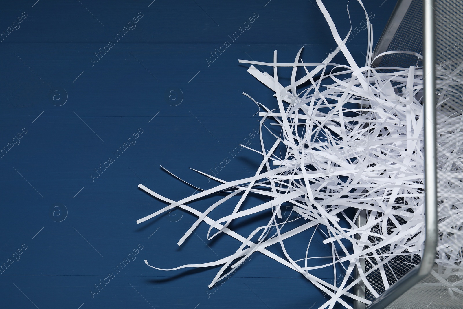 Photo of Shredded paper strips in trash bin on blue wooden table. Space for text