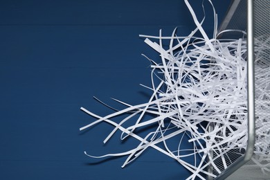 Photo of Shredded paper strips in trash bin on blue wooden table. Space for text