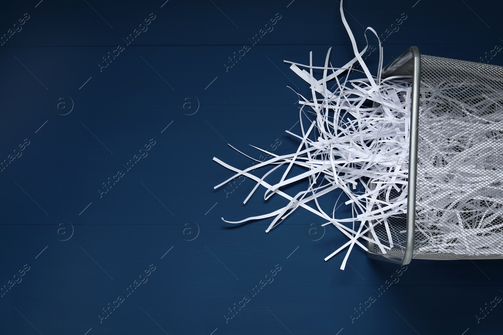 Photo of Shredded paper strips in trash bin on blue wooden table, top view. Space for text