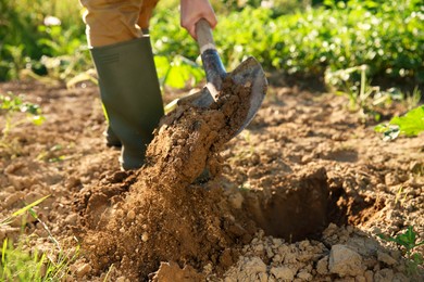 Photo of Farmer digging soil with shovel on sunny day, closeup