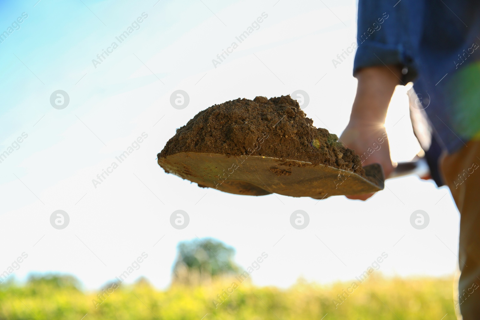 Photo of Farmer digging soil with shovel on sunny day, closeup. Space for text