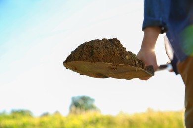 Farmer digging soil with shovel on sunny day, closeup. Space for text