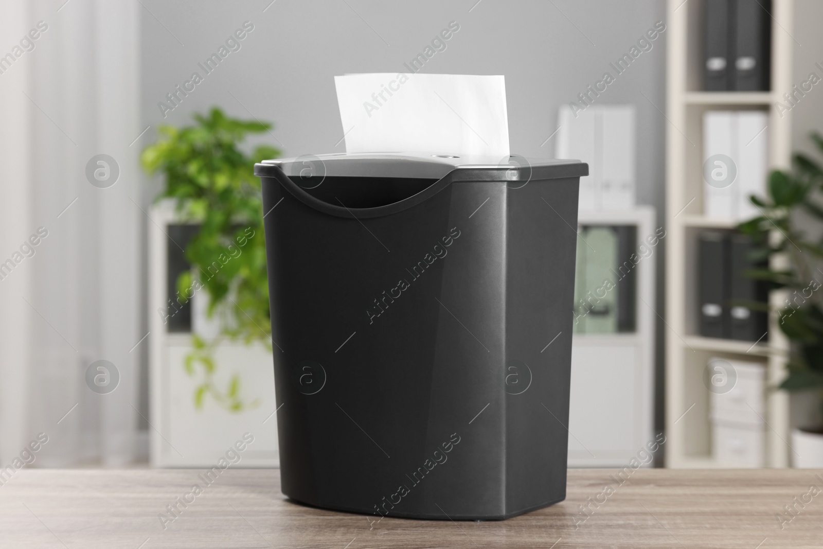 Photo of Destroying sheets of paper with shredder on wooden table in office