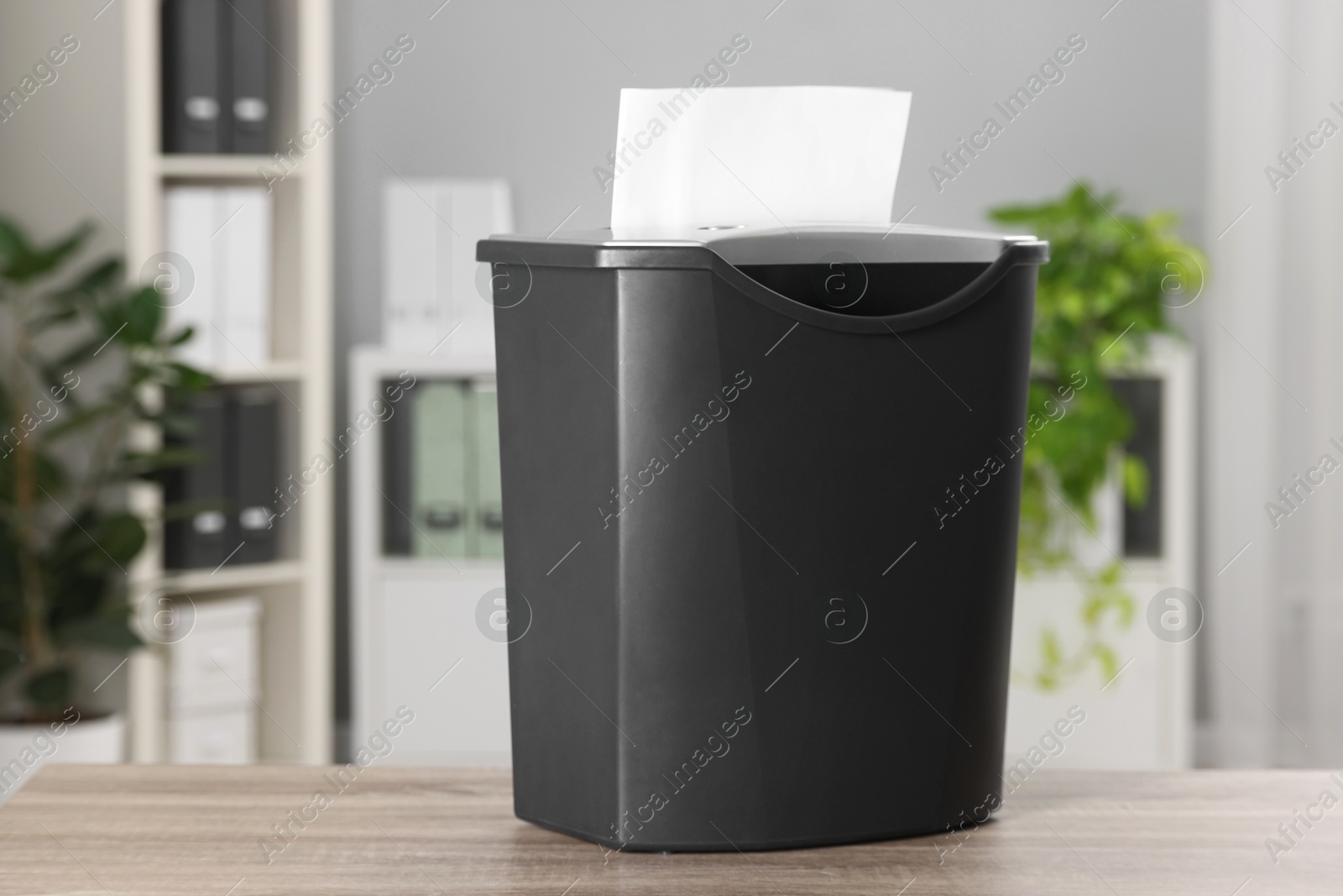 Photo of Destroying sheets of paper with shredder on wooden table in office