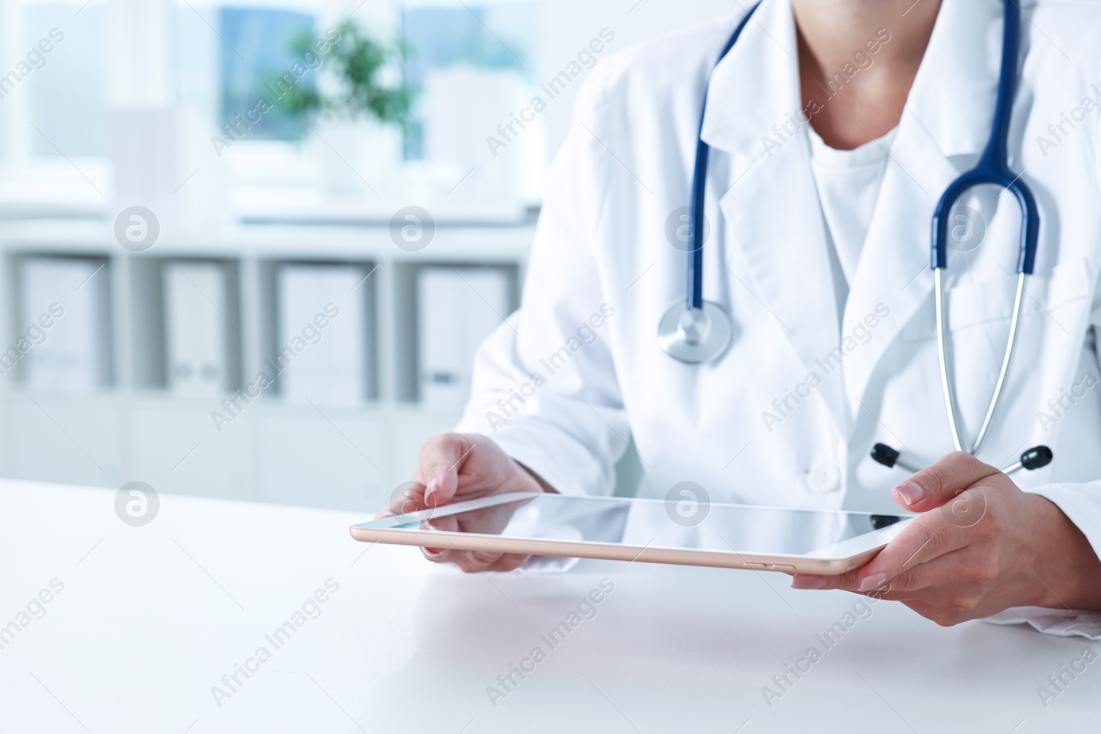 Photo of Doctor with tablet at table in clinic, closeup view