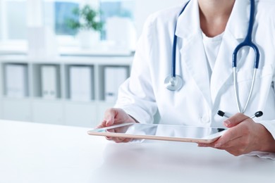 Photo of Doctor with tablet at table in clinic, closeup view