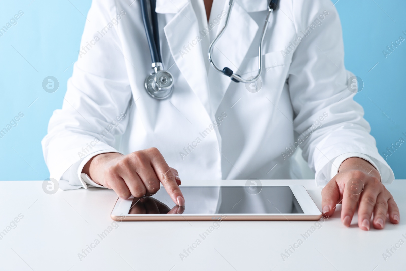 Photo of Doctor with tablet at table against light blue background, closeup view