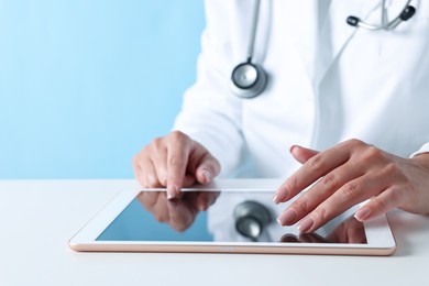 Photo of Doctor with tablet at table against light blue background, closeup view