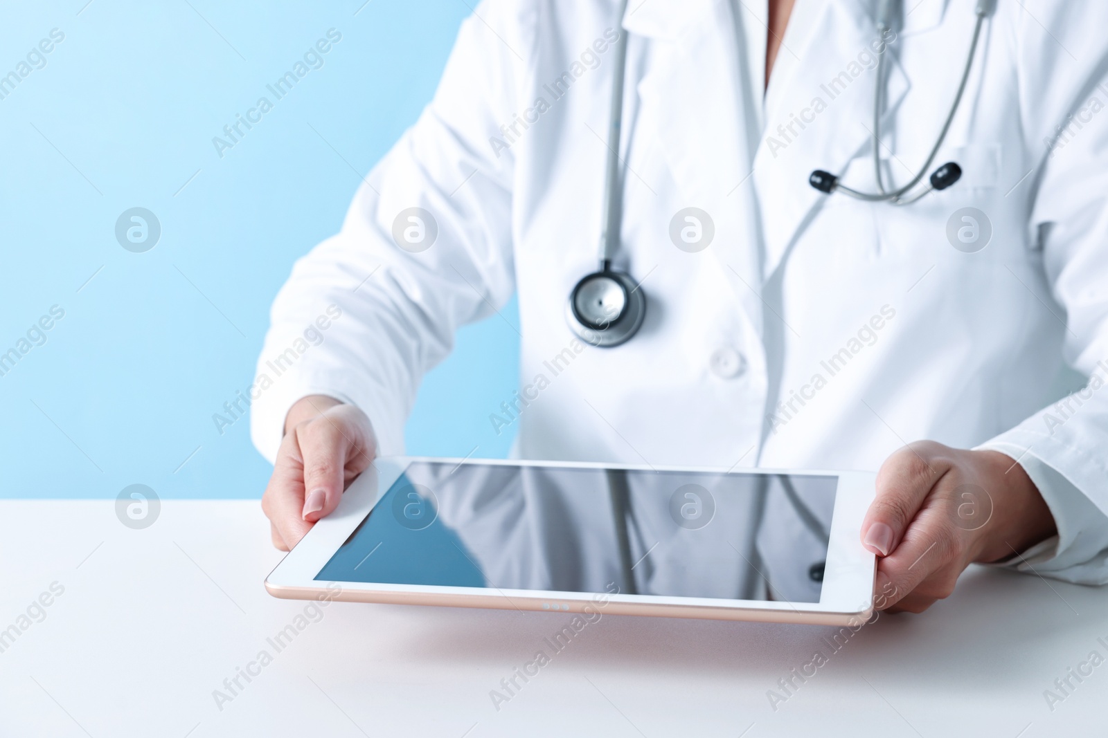 Photo of Doctor with tablet at table against light blue background, closeup view