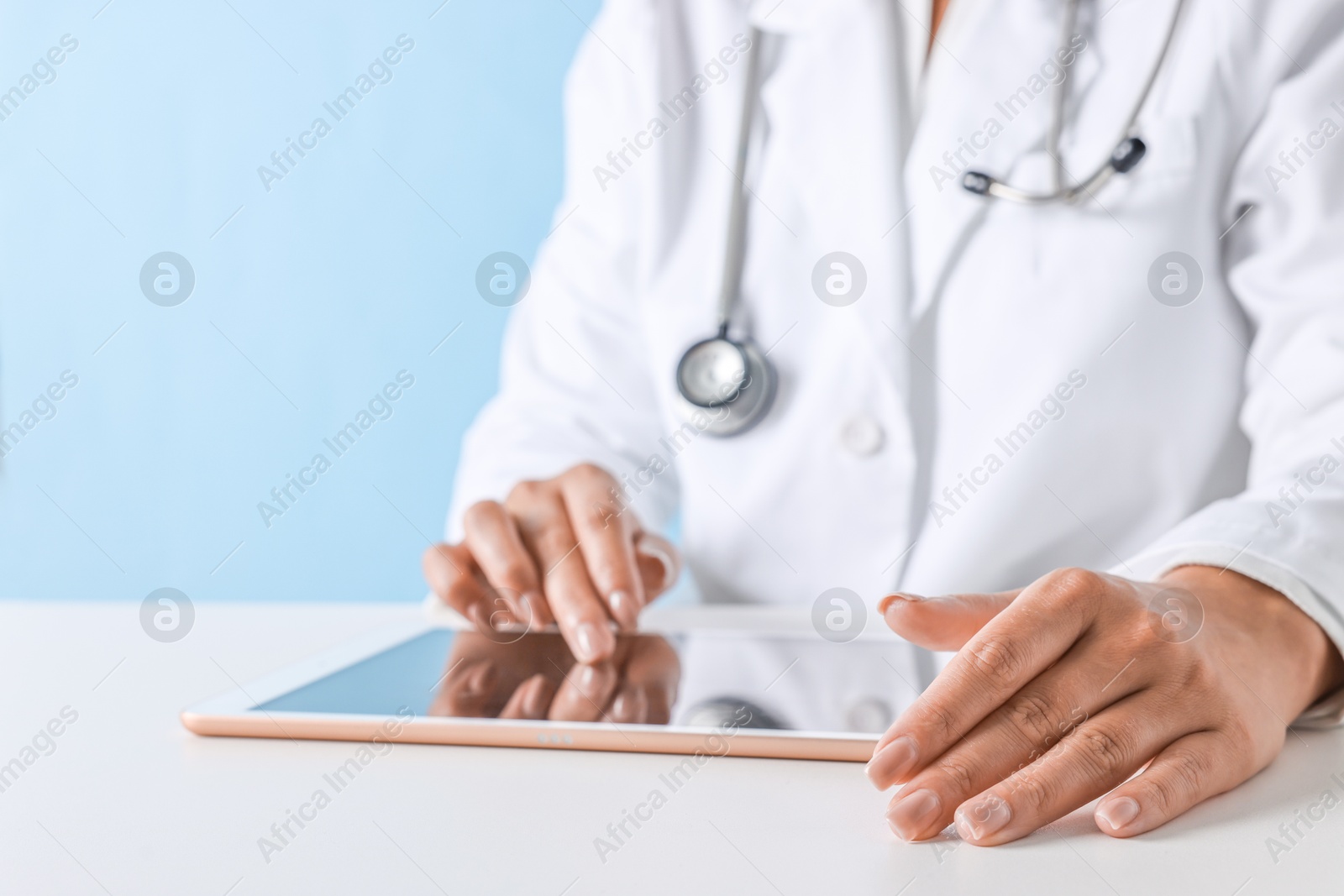 Photo of Doctor with tablet at table against light blue background, closeup view