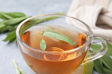 Aromatic herbal tea in cup with sage on grey table, closeup