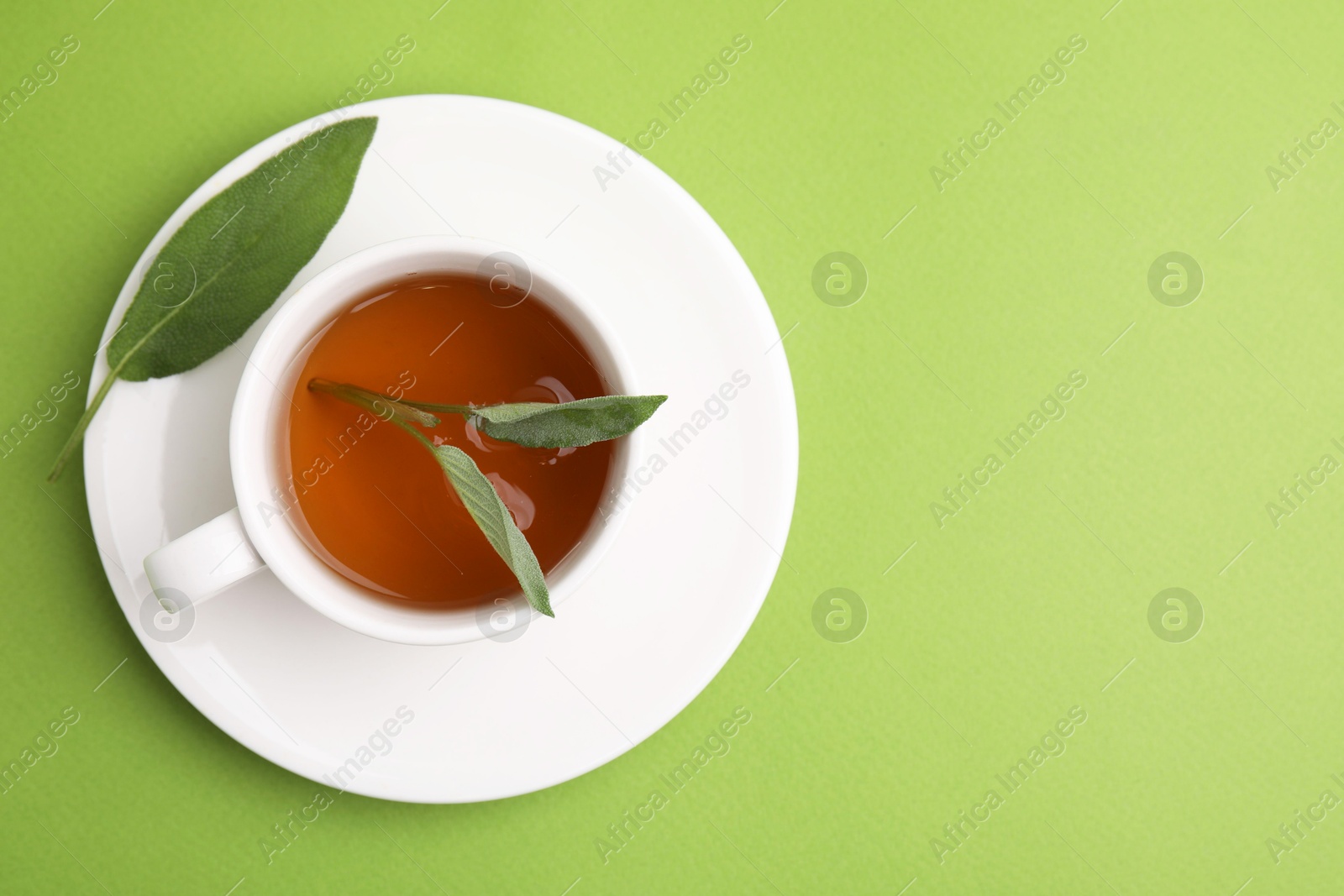 Photo of Aromatic herbal tea in cup with sage on green table, top view. Space for text