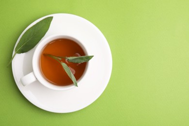 Aromatic herbal tea in cup with sage on green table, top view. Space for text